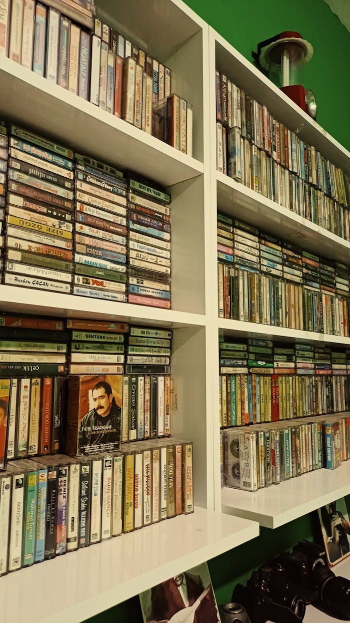A large collection of vintage cassette tapes organized on white shelves.